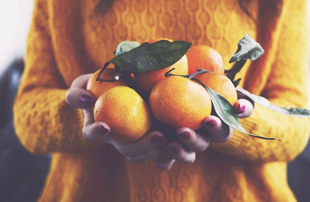 Femme avec un pull orange tenant des clémentines dans ses mains