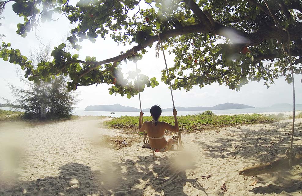 Femme se balançant sur une balançoire suspendue à un arbre sur la plage