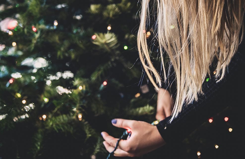 Femme tenant une guirlande lumineuse à côté d'un sapin de Noël